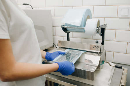 Dentist's assistant hands in gloves packing dental instrument set for autoclaving in a plastic bag using vacuum packing machine. Sterility and safety care conceptの写真素材