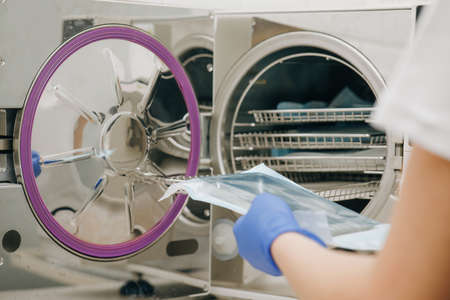 Medical Sterilizer Interior. Medical autoclave for sterilising surgical and other instruments. Young Female Dentist Places Medical Autoclave For Sterilising Surgical And Other Instrumentsの写真素材
