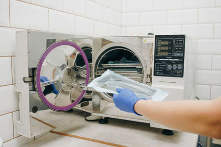 Assistant with sterile dentist tools. Sterilizing medical instruments in autoclave. Dental office.の写真素材