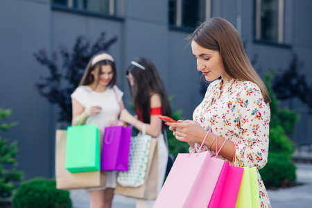 Sale, consumerism, technology and people concept - happy young women with smartphones and shopping bags.の写真素材