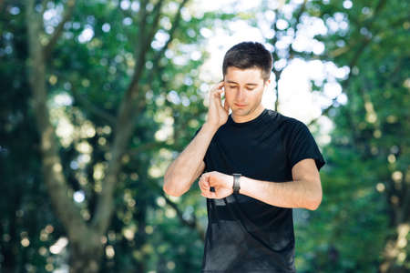 Adult man running outdoor using wireless earphones listening to music with smartwatch enjoying healthy. Male runner working out cardio exercise workout in city parkの写真素材
