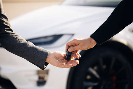Car Salesman Finishing Up Dealing Car. Young Happy Man Receiving Car Keys to Her New Automobile. Dealer giving key to new owner in auto show or salon.の写真素材