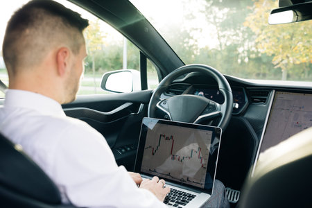 Successful businessman in formal outfit opening personal laptop while sitting in modern car. Bearded...