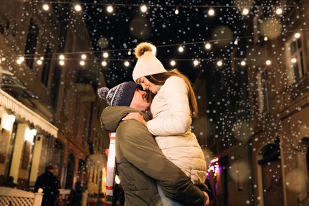 Christmas gifts exchange. Xmas celebration together. Smiling couple celebrating Xmas eve together at bright garland decoration.の写真素材