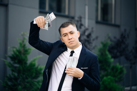 Man shows money and celebrating success, victory while looking to camera. Outdoors. Amazed happy excited businessman with money - U.S. currency dollars banknotesの写真素材
