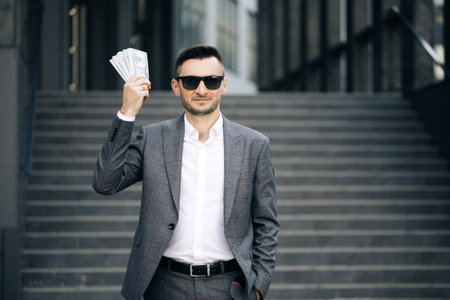Lifestyle, richness, joy, success. Happy rich successful man holds dollars outdoors. Portrait of satisfied businessman holds money.の写真素材