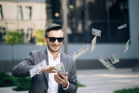 Successful Businessman in a Suit Wear Sunglasses Throwing Money in the Camera Standing in the Street near Office Building. Money rain, falling dollars. Successful business conceptの写真素材