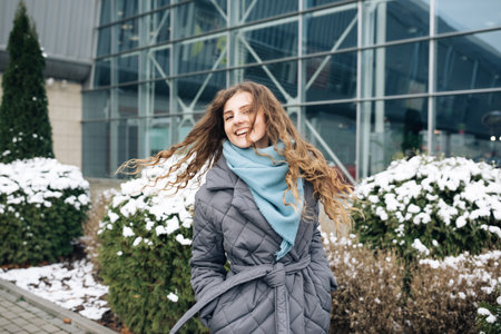 Charming young curly woman with a magnificent brown hair, big brown eyes and stylish look turns to camera and smiles. Attractive young lady is rushing in the winter city-centerの写真素材