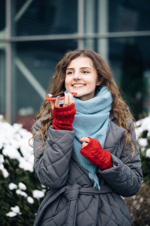 Portrait of Curly-haired Woman with phone using the voice recognition ai audio message on the phone, audio message ai speech helper. Vacation winter outdoorの写真素材