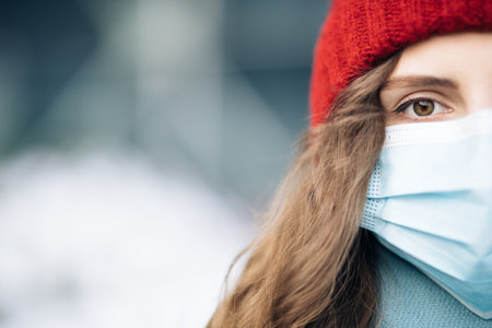 Close up of female half face at street . Portrait of caucasian woman looking at camera. Curly haired woman wears protective mask to avoid contaminating coronavirus. Health and safety conceptの写真素材