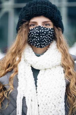 Portrait of a woman with brown curly hair out and about in the city streets during the day, wearing a face mask against air pollution and Coronavirus Covid19, looking at camera.の写真素材