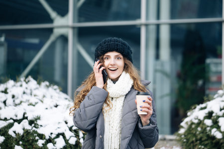 Excited woman winner screaming yes rejoicing success at cellphone. Portrait of young curly woman in winter clothes holding phone celebrate good mobile news surprise bidの写真素材
