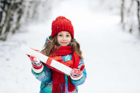 Child holding gift box and surprise face. Little girl with christmas box gift in winter outdoors on Xmas eve. Happy Little caucasian girl smile and holding gift box in Christmas dayの写真素材