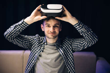 Young man using VR headset for watching the 360 video while sitting on sofa at home . Close up man using modern 3D vr glasses. Augmented Realityの写真素材