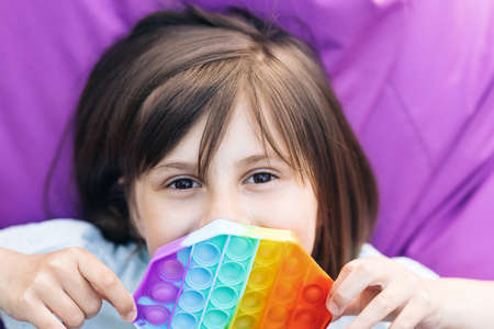 Trendy antistress sensory toy fidget push pop it and simple dimple in kids hands. Close up of portrait little girl with a modern popit toy. Colorful and bright pop it toy simple dimpleの写真素材