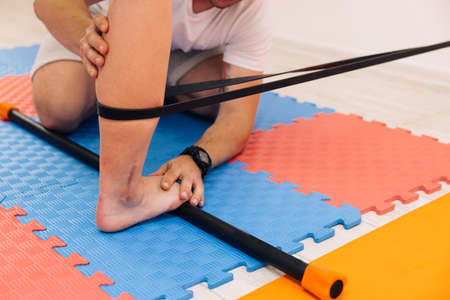 Adult male physiotherapist treating the foot of a female patient. Woman with elastic bandage on knee doing sport exercises in gym. Physio gives myotherapy using trigger points on athlete woman.の写真素材