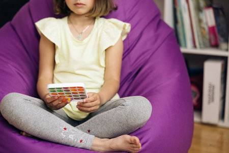 Little girl with a modern popit simple dimple snapperz toy. Colorful and bright toy. Simple dimple. Child is sitting on chair with colorful trendy antistress sensory toy pop it simple dimple snapperzの写真素材