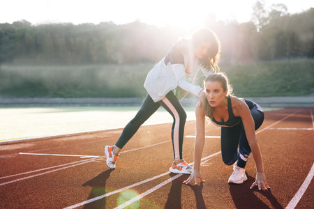 Young female runner with personal trainer preparing for blasting off in mist on sports track of...