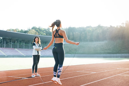 Caucasian woman with personal trainer jumping rope as part of her fitness workout. Sporty female...