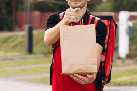 Food delivery man order from a restaurant. Handsome young man in a T-shirt and a cap. Happy delivery worker holding packet with food smiling. Delivery service door to doorの写真素材