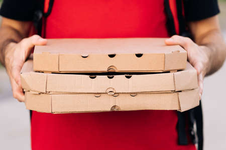 Close-up of the couriers hands and pizza. Portrait of delivery man holding cardboard pizza box against city, courier food delivery. Delivery man holding boxes with hot pizza, food order onlineの写真素材
