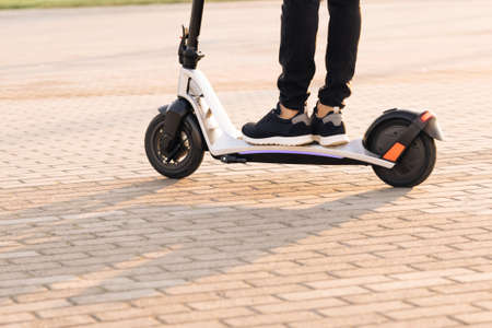 Shot on legs young man in black sneakers ride on electric mobile scooter at sunset. Eco-friendly transportation. Fast speed driving electric transport. Man hipster riding an electric scooterの写真素材