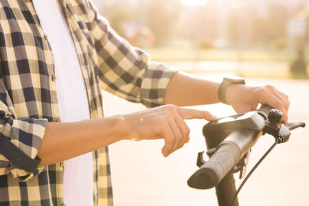 Close up of hipster man turns on the electric scooter. Male is pushing start button of modern gadget and driving along street of city. Hands of a young man close-up. Ecological alternative transportの写真素材