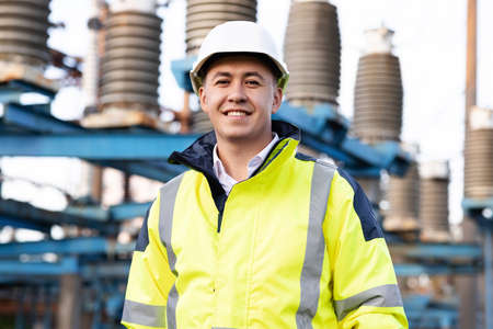 Industrial people. Sustainable energy. Portrait of asian ecology worker in hard hat standing at high voltage power station. Technologyの写真素材