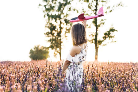 Girl with the airplane in the hands at sunset. Happy girl with a toy airplane on a lavender field in the sunset light. Children play toy airplane. Concept big child dream.の写真素材