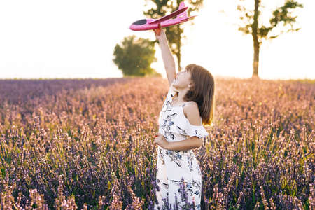 Children play toy airplane. Girl with the airplane in the hands at sunset. Happy girl with a toy airplane on a lavender field in the sunset light. Concept big child dream.の写真素材