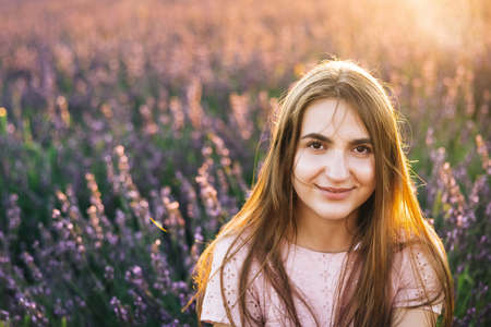 Beautiful woman is posing at field of purple lavender flowers. Beautiful woman in the lavender field on sunset in France .Girl collect lavender. Soft focusの写真素材