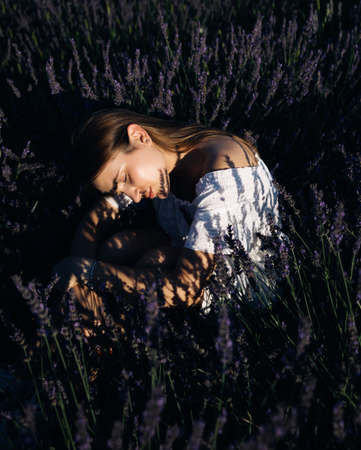 Beautiful girl in lavender field on sunset in France. Romantic woman in fairy field of lavender. Young woman in dress outdoorsの写真素材