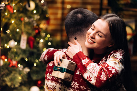Happy woman embracing her boyfriend and hugging him near decorated glowing fir tree. Romantic winter...
