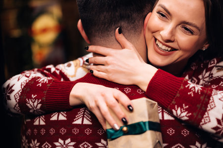 Young happy woman embracing her boyfriend and hugging him near decorated glowing fir tree. Romantic winter story. Happy wife feels grateful hugs husband express gratitude for New Year giftの写真素材