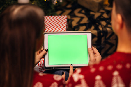 Hands holding a tablet computer with green mock up screen. Caucasian couple using tablet for...