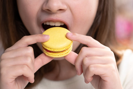 Close up of gorgeous school girl biting french macaroon, enjoying eating, confectionary desire and...