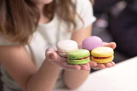 Childs hands taking French macarons of colorful macarons isolated on white table. Kid girl plays macarons cookie. Dessert person, sweet tooth, gourmetの写真素材