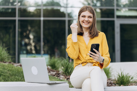 Joyful girl reading good news on phone. Surprised lady celebrating victory on smartphone outdoor....