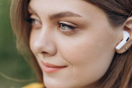 Close up face portrait of a lovely young fitness girl listening to music through wireless earphones outdoorsの写真素材