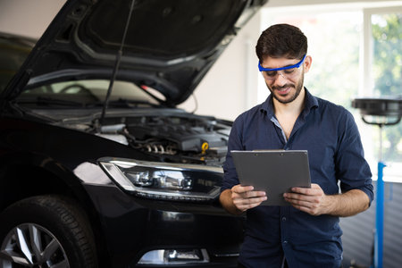 Mechanic inspects the car undercarriage way and makes a note on his inspection sheet. Automobile service, car mechanic. Car service employe inspect car. Modern workshop.の写真素材