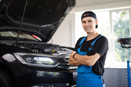 Portrait happy mechanic worker in blue uniform and cap from auto service center in front of the camera looking straight smiling and enjoying the time at his work placeの写真素材