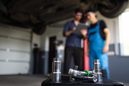 Male Mechanic Talking to Manager Under Vehicle in Car Service. Specialist is Showing Info on a Tablet Computer. Empowering Man in Modern Workshopの写真素材