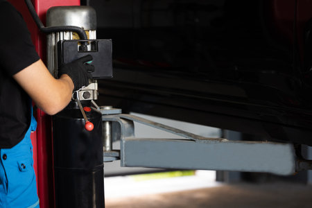 Man hand car mechanic lifts car in vehicle service center. Male car mechanic at work in spacious garage. Mechanic works in car repair shopの写真素材