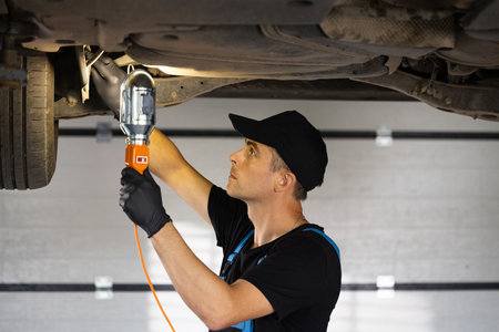 Male car mechanic checking car. Auto mechanic working underneath car lifting machine at the garage. Working in car repair shop and running small feminine business conceptの写真素材