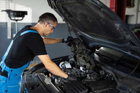 Car mechanic noting repair parts during open car hood engine repair at garage. Mechanic man open a car hood and check up the engine. Overheating of a car engine. Motor with open hoodの写真素材