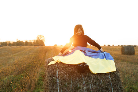 Portrait of little girl holding a yellow and blue flag of Ukraine on a background of sunset sky. Stop war in Ukraine. Russia stop war. Kid outdoors. International day of democracy conceptの写真素材