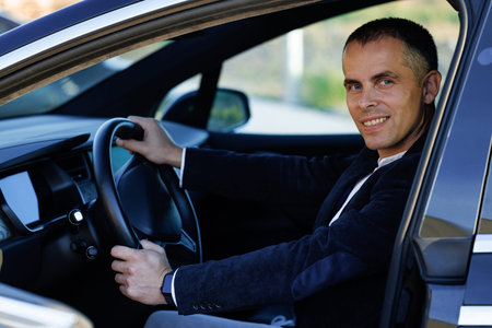 Portrait of handsome businessman smiling while driving a new car. Young handsome man is sitting in...