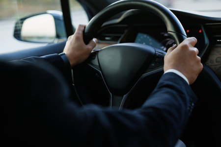 Man driving with his two hands on steering wheel. Business man driving in his modern electric car....