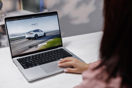 CALIFORNIA, USA - NOVEMBER 14, 2022: Tesla website, buying a car online. Woman using laptop computer ordering Tesla model X Plaid and full self-driving autopilot. Screen with Website Tesla Companyのeditorial素材