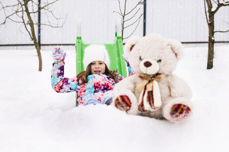 Cute toddler girl playing with teddy bear in winter park. Winter portrait of little caucasian child girl. Outdoor winter activities for kidsの写真素材
